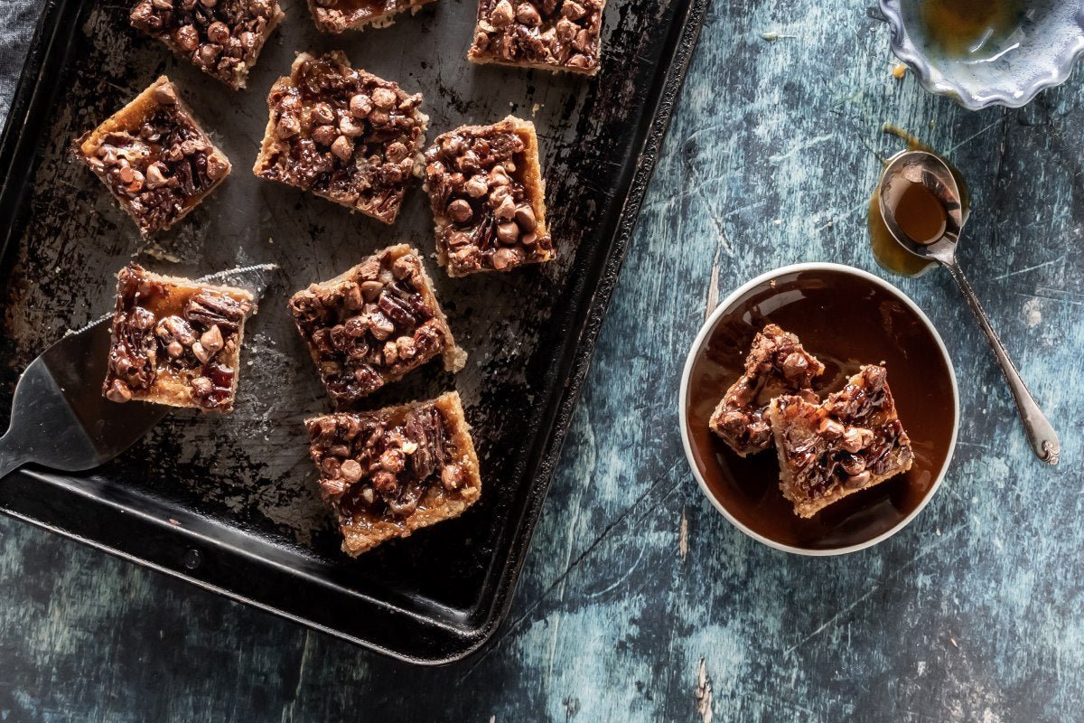 Freshly baked pecan pie bars cut into squares on a dark pan with caramelized pecans